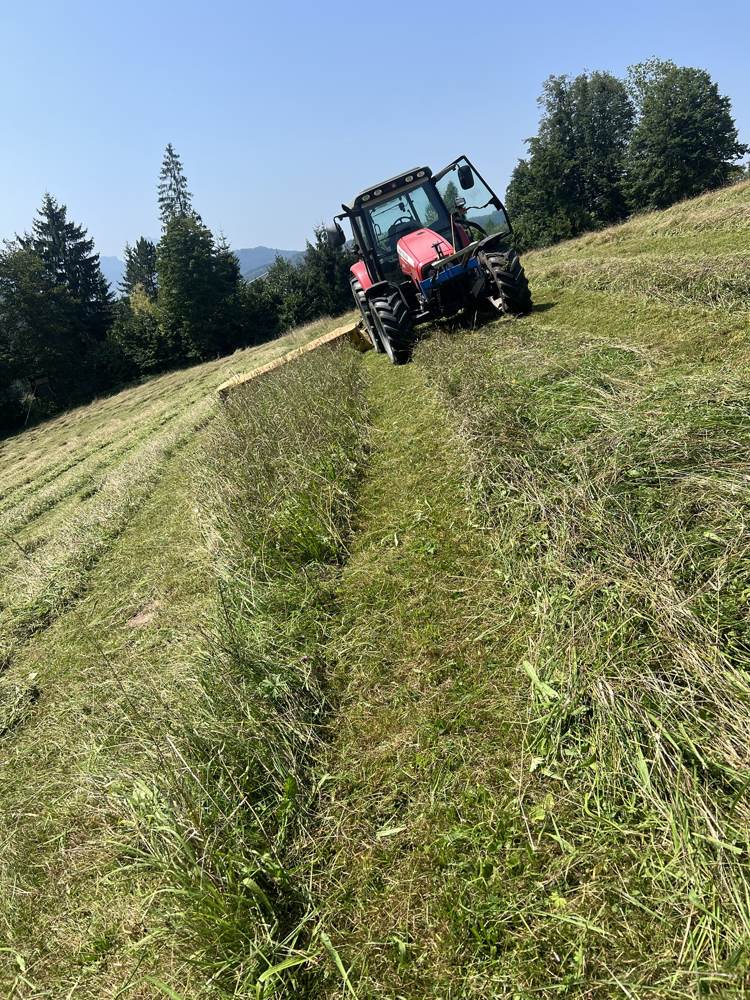 Traktor mäht eine Wiese am Hang